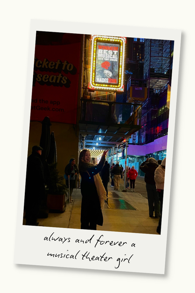 Woman in front of the Walter Kerr Theater in New York pointing to a marquee with a poster for the musical "Hadestown." A Polaroid frame surrounds the photo, and text on the frame reads "always and forever a musical theater girl."
